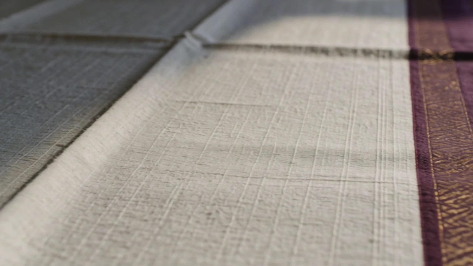 Warm light moves across woven cloth and its wine-coloured border.